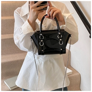Detail of black patent leather mini handbag with silver hardware and chain strap