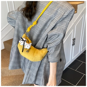 Detail of yellow suede croissant bag with cute puppy charm worn over a grey blazer