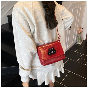 Detail of red glossy crossbody bag featuring a plush cartoon cat and embossed letters