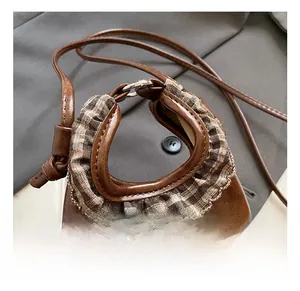 Detail of a brown leather cloud bag featuring a plaid ruffle handle and metal ring