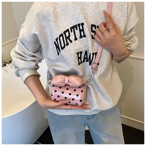 Pink polka dot mini crossbody bag with large bow detail and glossy finish shown on model