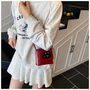 Detail view of the red glossy leather crossbody bag with a cute black cat patch
