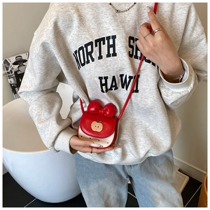 Détail du mini sac bandoulière pomme rouge à pois montré sur un jeune mannequin