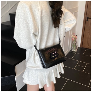Detailed view of black cartoon cat crossbody bag worn with a casual outfit