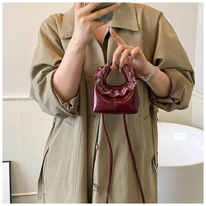 Close-up of a mini burgundy handbag featuring a stylish red plaid ruffle handle detail