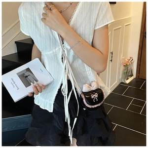 Close-up of mini black patent leather crossbody bag with pink bow and ruffled lace details