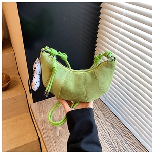 Detail of green suede croissant bag for kids featuring a plush puppy charm and knot strap
