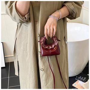 Mini wine red glossy handbag with checkered ruffle handle shown on a beige trench coat