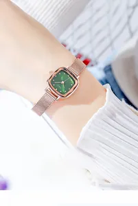 Close-up of rose gold Milanese mesh band and emerald green square dial watch on wrist