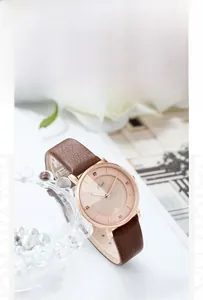Orologio in pelle marrone con cassa oro rosa e quadrante rosa accanto a perle e fiori
