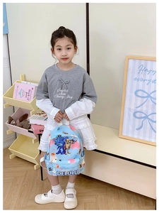Close-up of cute light blue kids backpack with cartoon prints held by a young girl
