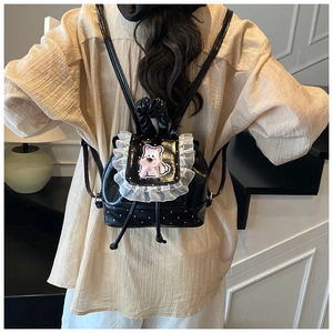 Detail of black glossy mini backpack featuring white lace trim and cute bear patch