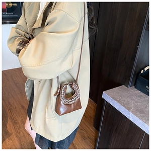 Detail of a brown round crossbody bag with plaid ruffle trim and slim shoulder strap