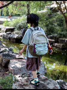 Kids outdoor backpack with multi-color splicing design shown in a forest stream setting