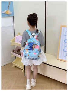 Light blue kids backpack with cartoon prints shown on a child in a cozy room