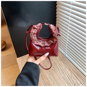 Detail of burgundy mini leather bag featuring a red grey plaid ruffle trim and thin strap