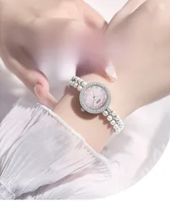 Détail du cadran en nacre rose et du bracelet en perles blanches de la montre