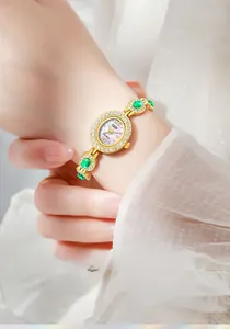 Elegant gold quartz watch detail featuring oval dial and green emerald gemstones