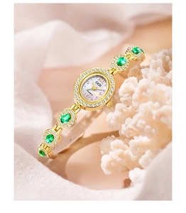 Detail of GEDI gold watch featuring green emerald-cut stones and crystal-set bracelet