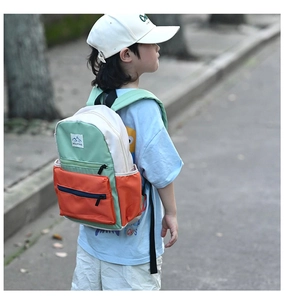 Outdoor shot of a color-block kids backpack with green, cream, and orange paneling detail