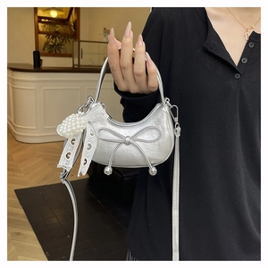 Close-up of silver mini handbag with metallic bow, pearl lace charm and crossbody strap