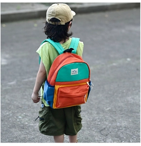 Outdoor shot of a multi-color kids backpack featuring bold red blue and green nylon panels