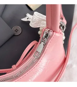 Detail of silver zipper on pink wrinkled leather bag with white lace bow and pearls