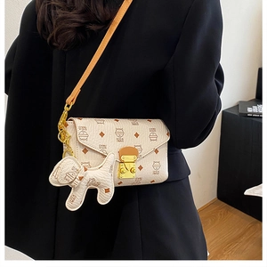 Détail du sac enveloppe beige à imprimé chaton avec fermoir doré porté par le mannequin