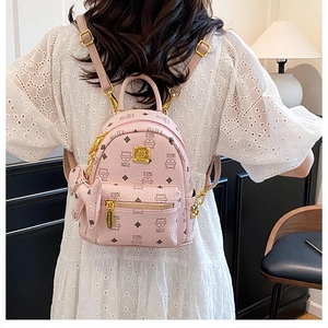 Close-up of pink mini backpack with monogram print and bow detail on female model