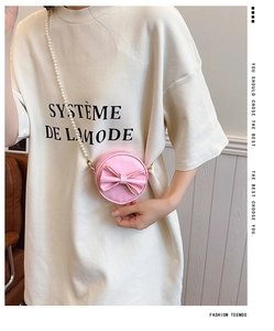 Gros plan du mini sac rond rose avec nœud et bandoulière en perles blanches sur modèle