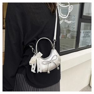Detail of silver crescent mini bag with bow and pearl lace charm on a model