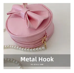 Détails d'un mini sac rond rose avec décoration de nœud et bandoulière en perles