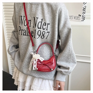 Detail of red mini crossbody bag featuring decorative bow and pearl lace pendant