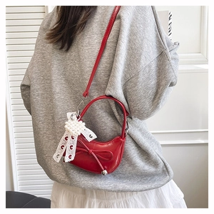 Red patent leather crescent bag with pearl bow charm worn on person for size view