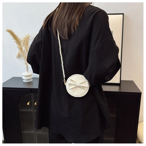 Détail du petit sac rond blanc avec nœud décoratif et bandoulière en perles élégante