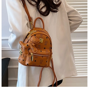 Mini brown backpack with bear charm and chic monogram print worn by a model in a suit