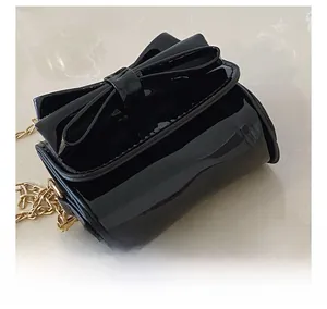 Detail of glossy black patent leather mini bag with large bow and gold chain strap