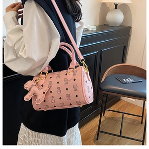 Pink cylinder boston bag with cat print and charm shown worn by a model in a room