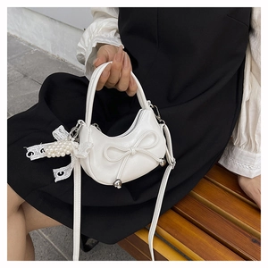 Detail of white half-moon bag with leather bow, silver metal accents, and pearl lace charm
