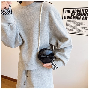 Détail d'un petit sac rond noir avec nœud papillon et élégante bandoulière en perles