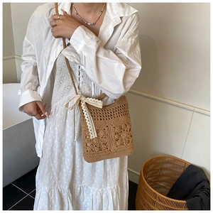 Detail view of woven straw crossbody bag featuring hollow floral pattern and lace bow strap