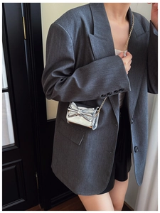 Detail of silver metallic mini bag with bow accent and gold chain on grey blazer