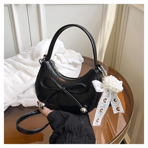 Detail of black crescent handbag featuring pearl pendant and lace bow accessory