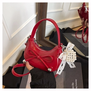 Detailed close-up of red patent leather handbag featuring a bow and pearl charm