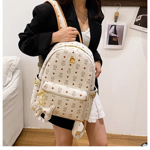 Détail d'un sac à dos crème avec imprimés marrons, clous dorés et breloque chien