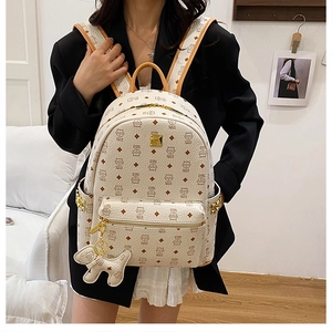 Détail d'un sac à dos crème avec motif de chat, fermetures dorées et breloque chien