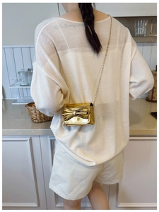 Mini gold bow shoulder bag with metallic finish and chain strap worn by a young model