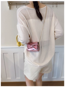 Pink patent leather mini crossbody bag with bow and gold chain on model's shoulder