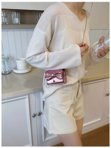 Pink metallic bow crossbody bag with gold chain strap shown on a model in a kitchen