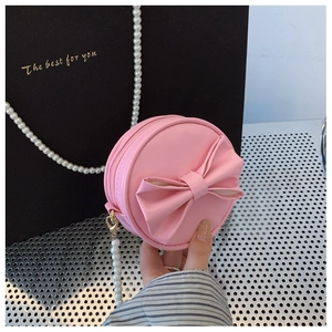 Détail d'un petit sac bandoulière rose pour fille avec nœud et chaîne en perles blanches